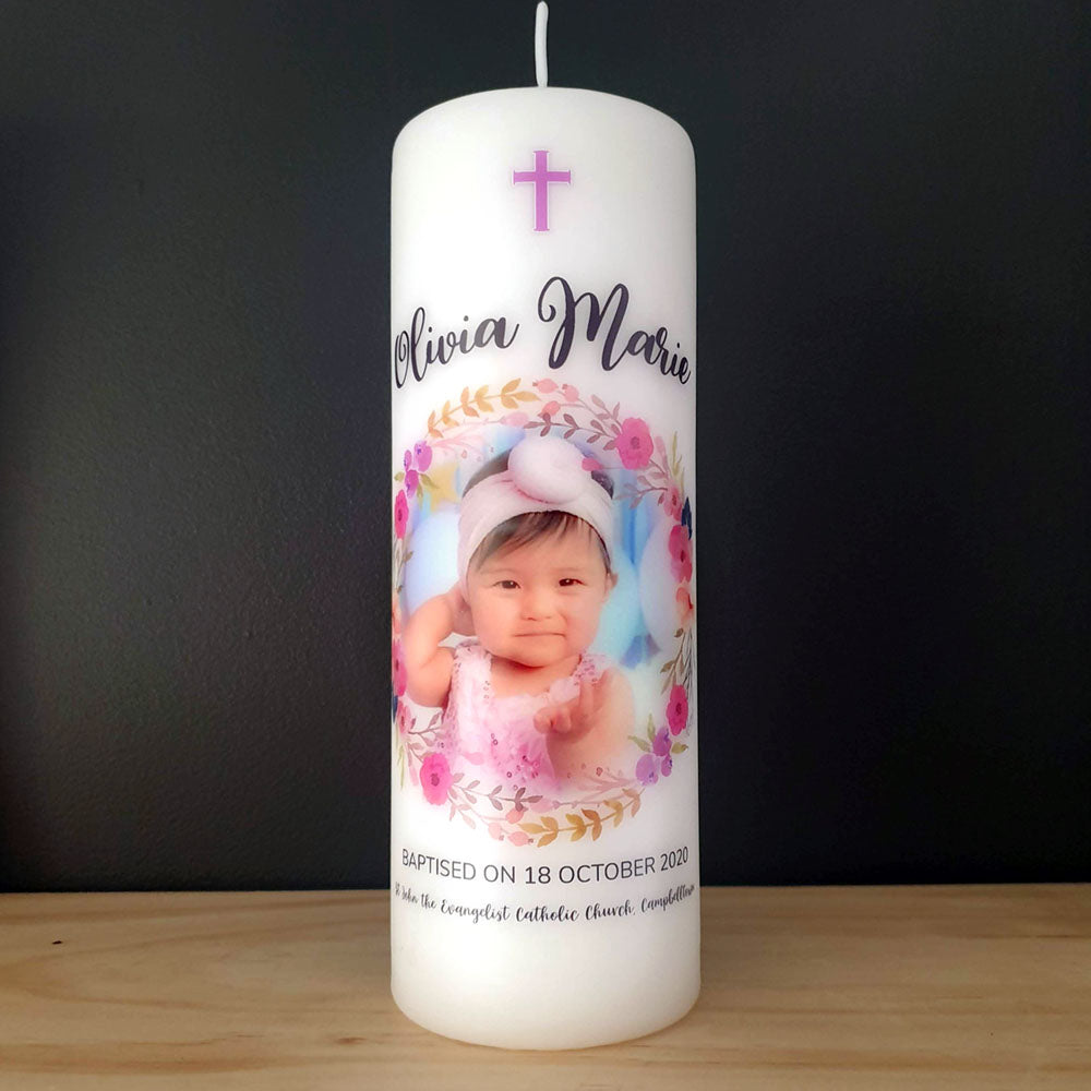 White Pillar Baptism candle with a pink and purple floral wreath, baby photo and name in black lettering