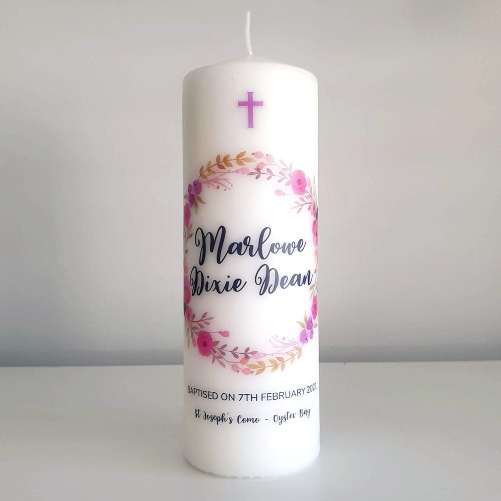 White Pillar Baptism candle with a pink and purple floral wreath and name in black lettering