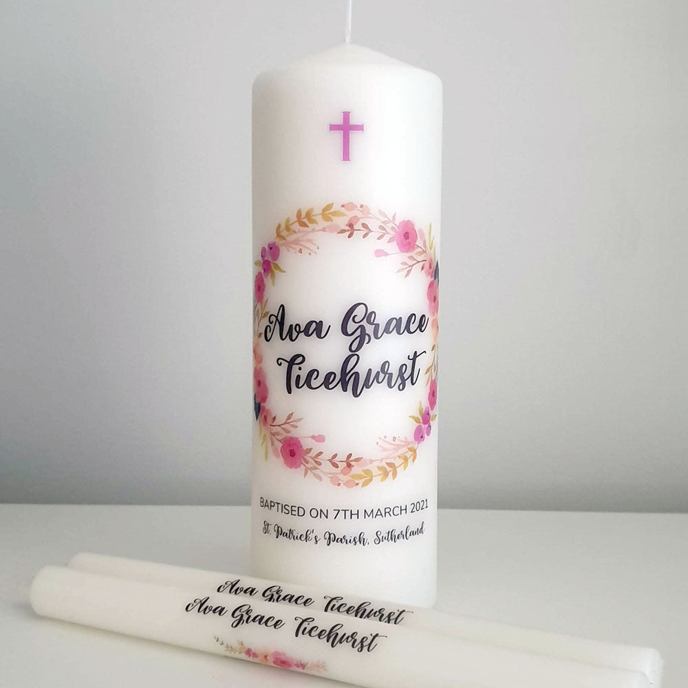 White Pillar Baptism candle with a pink and purple floral wreath and name in black lettering with two personalised taper candles
