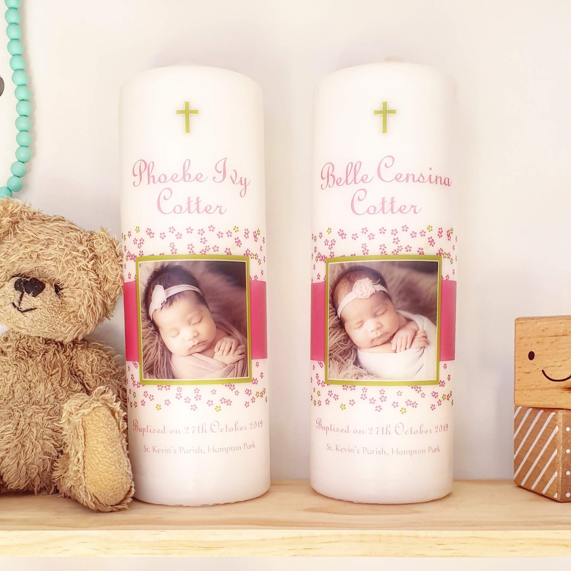 Two Baptism Candles with a photo of a baby and flowers on them with a teddy bear and 2 wooden toy blocks