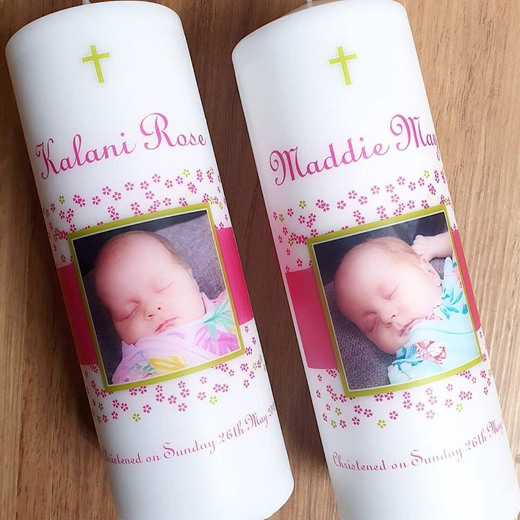 Two white pillar candles with a baby photo and flowers on them